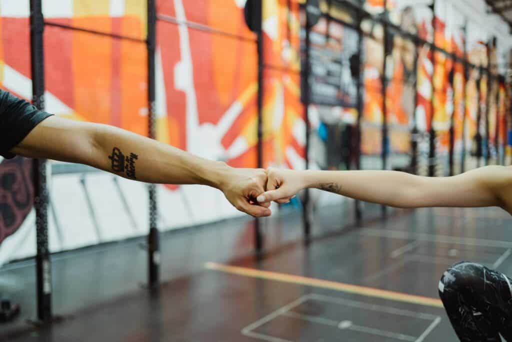 Two people fist bump in a colorful gym, symbolizing teamwork and healthy lifestyle.