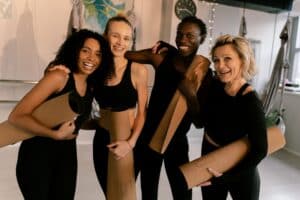 A cheerful group of diverse adults holding yoga mats in an indoor studio setting.